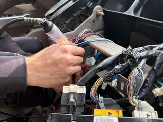 Close-up of Auto Electrician Using Test Light to Check Voltage and Diagnose Wiring Harness in Car Dashboard