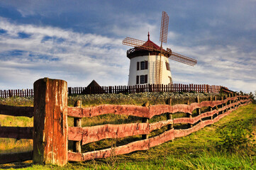 Gostków - Spokojny, kolorowy wiatrak na rustykalnym, drewnianym polu ogrodzonym pod złotym, czystym, błękitnym niebem o zachodzie słońca. © Pol Badger