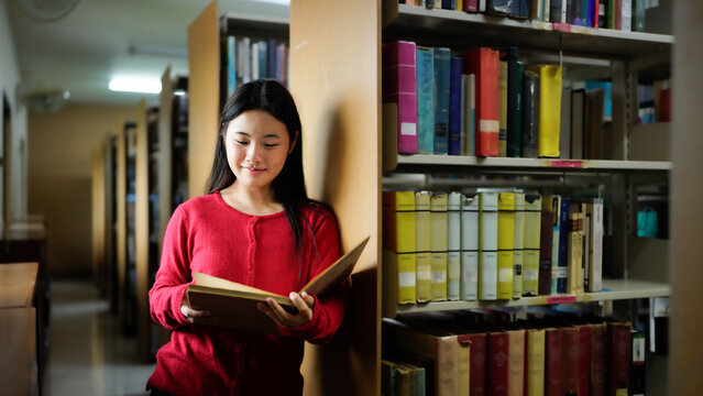 asian teenage woman reading book in a library for education, studying and research in school, university or college campus.