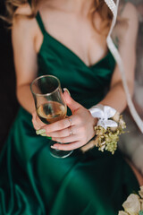 A photograph of a bridesmaid, a young woman, holding a glass of champagne with wildflowers and gold rings on her fingers.