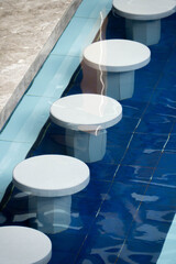 Modern circular stone stools submerged in a blue-tiled swimming pool, creating a minimalist and tropical resort aesthetic