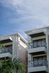 Modern tropical resort building with glass balconies, wooden accents, and palm trees beneath a bright blue sky