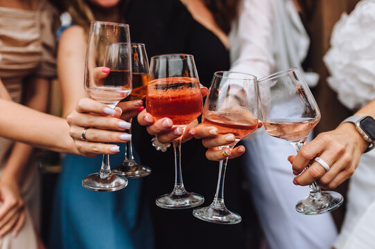 A close-up photo of women's hands holding glasses of alcoholic cocktails at a bachelorette party. Concept of female friendship.