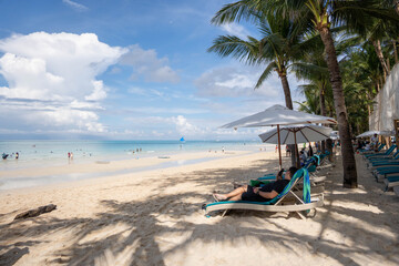 Tropical beach with palm trees, lounge chairs, and umbrellas overlooking turquoise sea under bright blue sky
