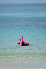 Person floating on turquoise sea with pink flamingo inflatable ring on a sunny beach day