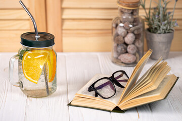 Relaxing indoor scene with a jar of refreshing citrus detox water, an open book, and eyeglasses on a rustic white wooden table