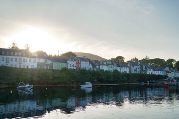 Fototapeta premium Scenic view of colorful houses along a tranquil waterfront in Ireland, with boats and calm water reflecting the buildings.