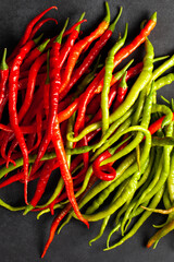Vertical image of red and green chili peppers arranged on a dark slate surface. Fresh organic spicy vegetables concept for cooking, food, and healthy eating themes.