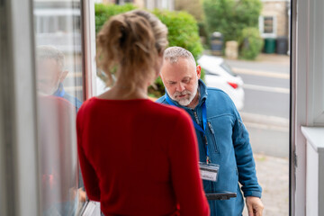 Delivery person hands over a package to a woman standing at her front door on a pleasant day