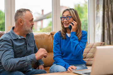 Two friends have a conversation while seated in a cozy living room with natural light and a laptop on the table