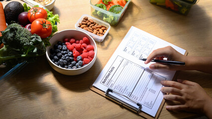 Nutritionist writing a healthy meal plan with fresh fruits, vegetables, and nuts on the table