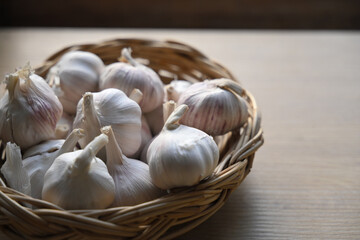 Close-up of fresh garlic bulbs in a woven basket on a wooden table, representing natural cooking ingredients