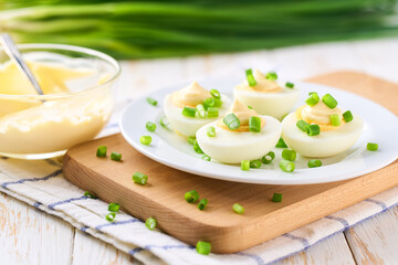 Fresh made snack, boiled chicken eggs with  mayonnaise and fresh green onions , on a wooden table, selective focus.