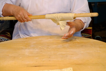 Close-up of a woman's hand rolling out flatbread dough with a rolling pin. Traditional Turkish pastries. Flatbread dough. A woman's hand rolling out dough with a rolling pin on a wooden table.