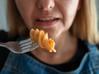 Woman holding fork and tasting creamy tomato pasta, close-up	