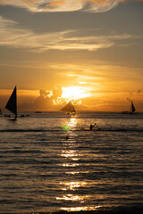 Sailboats gliding on calm sea during golden sunset with vibrant orange sky and reflections on water