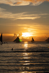 Sailboats gliding on calm sea during golden sunset with vibrant orange sky and reflections on water