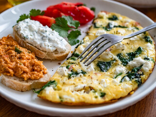 Healthy breakfast - omelette with feta cheese and spinach with sandwiches and tomatoes on wooden table	