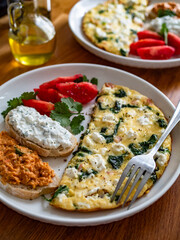 Healthy breakfast - omelette with feta cheese and spinach with sandwiches and tomatoes on wooden table	
