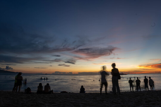 People watching colorful sunset on beach with calm waves and dramatic clouds over the ocean