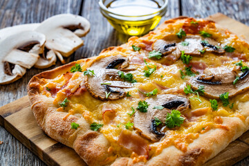 Mini pinsa with cheddar cheese, boiled ham and white mushrooms on wooden table