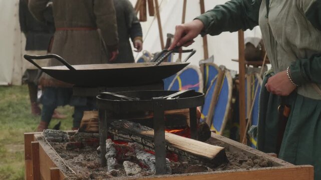 Hands of person moving flatbread in large special pan over open fire during traditional outdoor baking