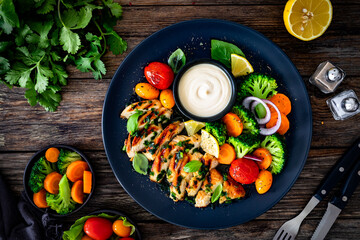 Grilled chicken breast, mayonnaise and vegetables on wooden table. Top view