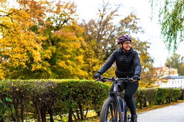Obraz premium Middle aged beautiful woman riding bicycle in city park in autumn. Front view 