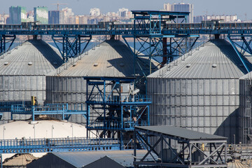 Close-up view of modern grain silos, conveyors and metal structures at agricultural factory. Industrial architecture, storage and processing of grain, farming infrastructure background.