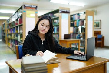 Young college woman working on his computer while studying in the library alone.