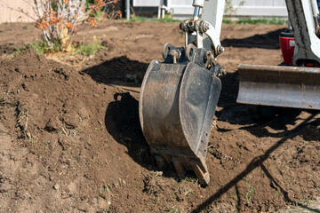 Backhoe bucket and blade working with fresh cut dirt in a small yard.