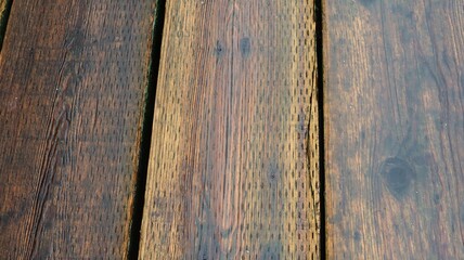 close up of weathered wooden planks which is a boardwalk with a wet rich brown color with visible grain patterns and small knots and moss growth in the gap