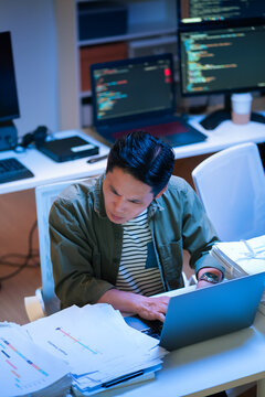 Asian programmer works late night office coding deep learning AI models, training neural networks with intense concentration and focus, dedicating overtime hours alone to machine learning development 