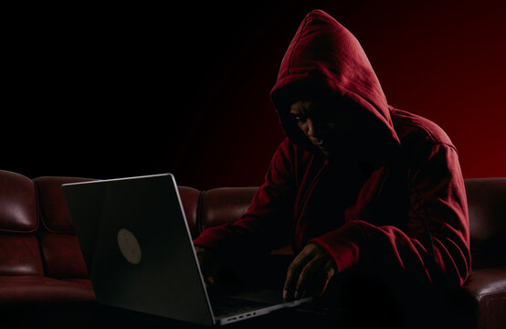 Hacker, coding and malware concept. Red hooded computer hacker in cybersecurity on the dark room background, metaverse digital world technology.