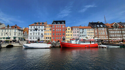 07 August, 2024, Copenhagen city center, Denmark Summer day scenic canal with boats and tourists, cyclists riding along colorful buildings and waterfront, vibrant urban atmosphere in European capital