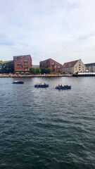 07 August, 2024, Copenhagen city center, Denmark Summer day scenic canal with boats and tourists, cyclists riding along colorful buildings and waterfront, vibrant urban atmosphere in European capital
