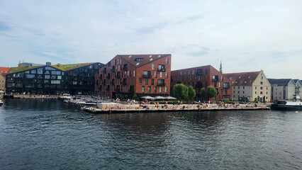 07 August, 2024, Copenhagen city center, Denmark Summer day scenic canal with boats and tourists, cyclists riding along colorful buildings and waterfront, vibrant urban atmosphere in European capital