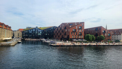 07 August, 2024, Copenhagen city center, Denmark Summer day scenic canal with boats and tourists, cyclists riding along colorful buildings and waterfront, vibrant urban atmosphere in European capital