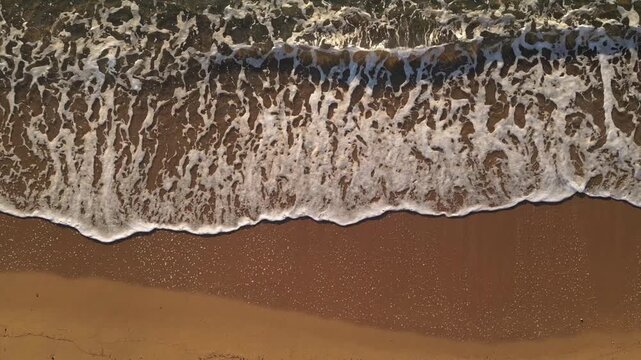 Slow motion drone footage of Mediterranean waves breaking on smooth sandy beach, detailed foam and surf pattern, cinematic coastal landscape background