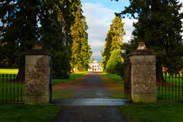 Pathway leading through a small gate to the majestic Emo Court House under cloudy skies