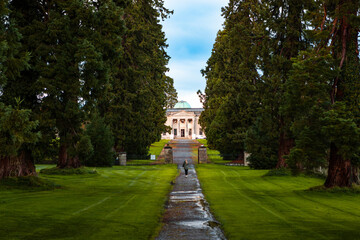 Woman walking along tree lined path toward Emo Court House on overcast afternoon in County Laois, Ireland