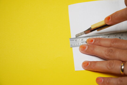 closeup of woman's hand cutting paper with cutter and ruler isolated on yellow background