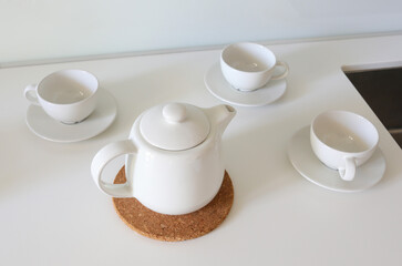 White teapot and cups on counter preparing herbal tea serving
