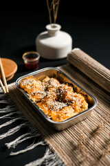 Close up of sesame dimsum baked with cheese topping in aluminum tray. Asian comfort food with creamy sauce and elegant minimal background for menu or promotion.