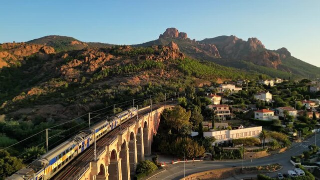 Aerial cinematic view of a train crossing the Antheor Viaduct in the Esterel Mountains near Saint Raphael, French Riviera, overlooking the Mediterranean Sea and luxury villas along the Cote dAzur at s