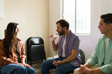 Fototapeta premium Distressed man drinking water to calm himself while attending group therapy meeting for support