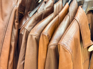 A collection of brown leather jackets hanging on a rack. The jackets are neatly arranged,...