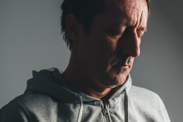 Low key portrait of mature man in casual clothing with eyes closed, expressing regret, sadness, and emotional reflection.