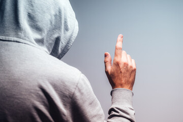 Rear view of man in gray hooded shirt raising index finger as if pointing or clicking on invisible virtual screen, tech concept.