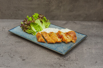 Sliced crispy chicken breast with creamy sauce and fresh salad on a ceramic plate.